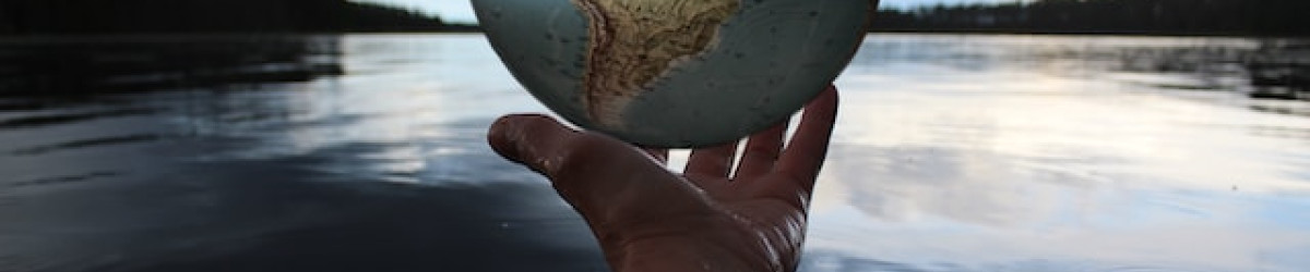 Person holding globe by a lake. Photo by Anne Nygård on Unsplash