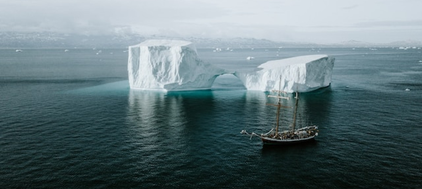 Schooner sailing by an iceberg in the Arctic. Photo by Annie Spratt on Unsplash