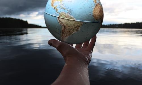 Person holding globe by a lake. Photo by Anne Nygård on Unsplash