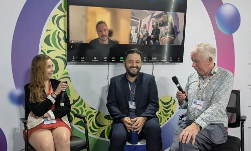 Three people with microphones, with one person behind on Zoom