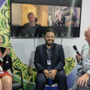 Three people with microphones, with one person behind on Zoom