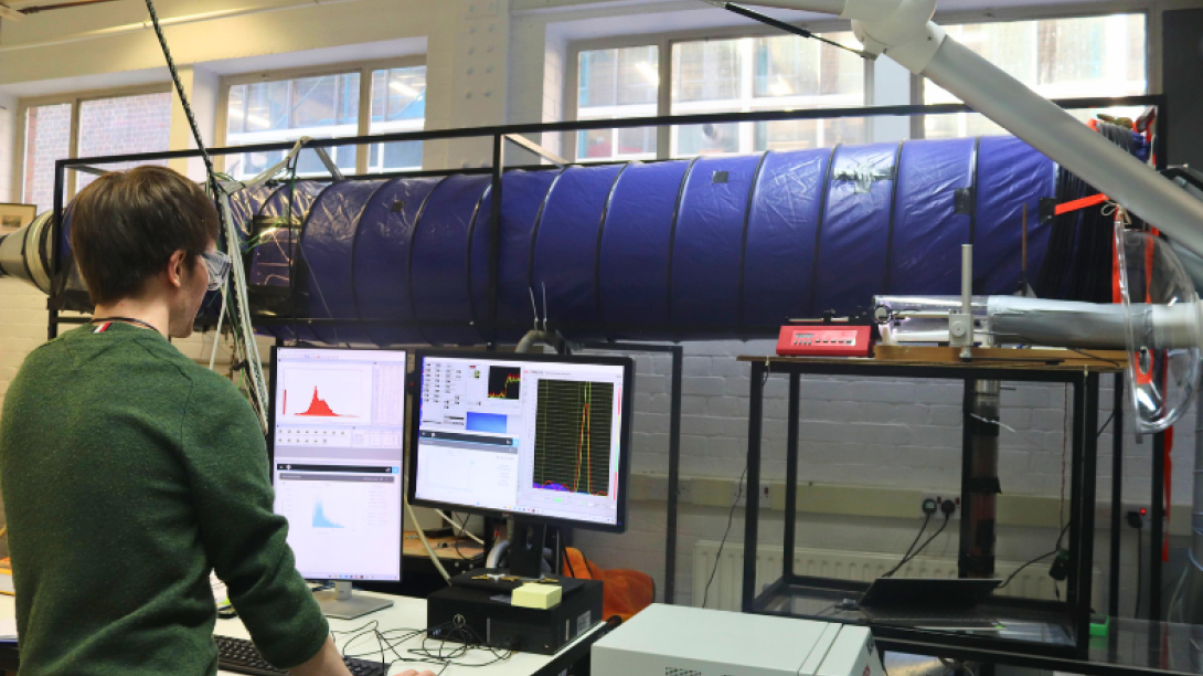 Researcher on computers in the lab in front of wind tunnel